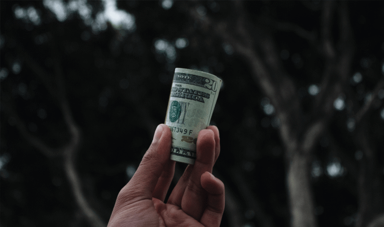 hand holding a roll of 20 dollar bills